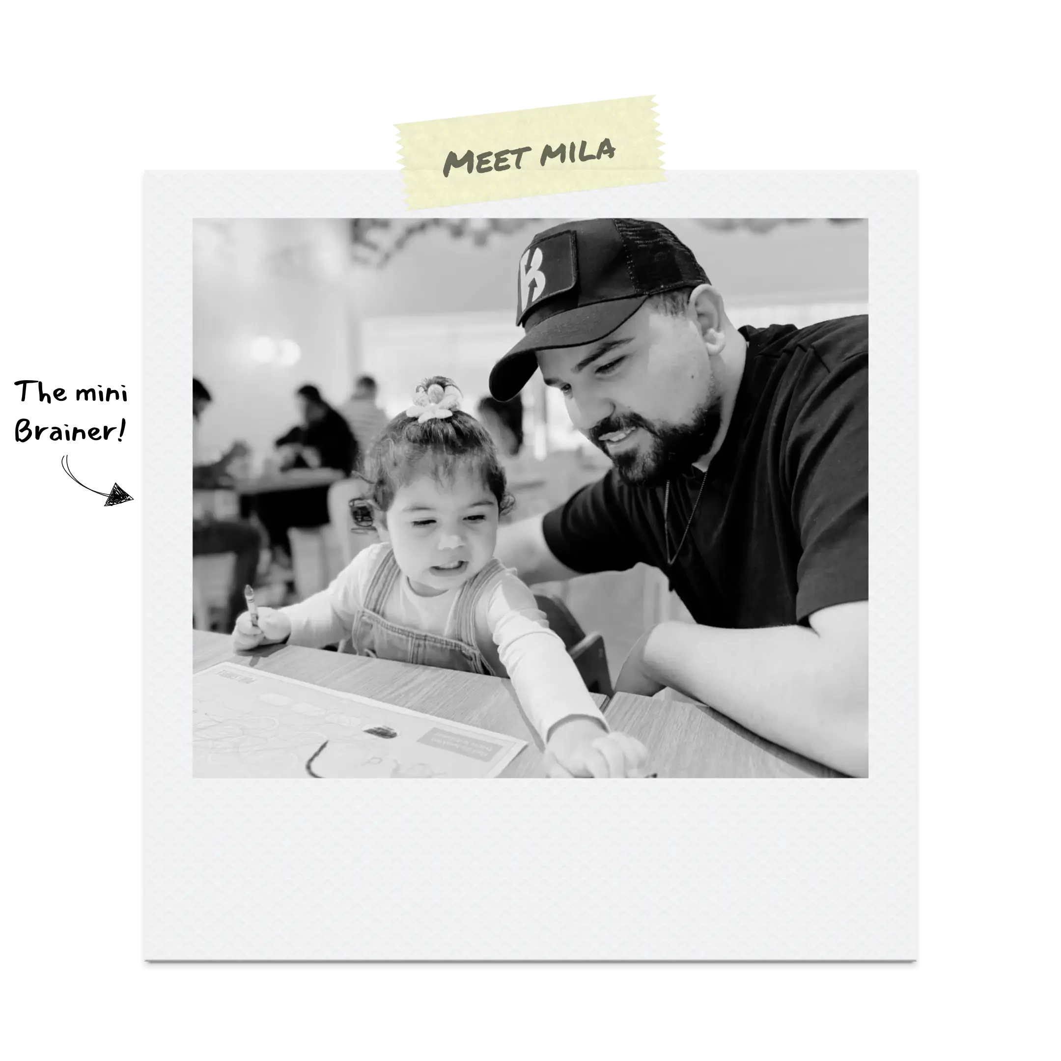 The Brainer smiling beside his daughter as she laughs and draws on paper.