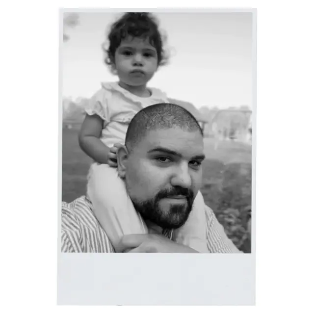 The Brainer holding his daughter with excitement and joy while she looks calm and unimpressed.